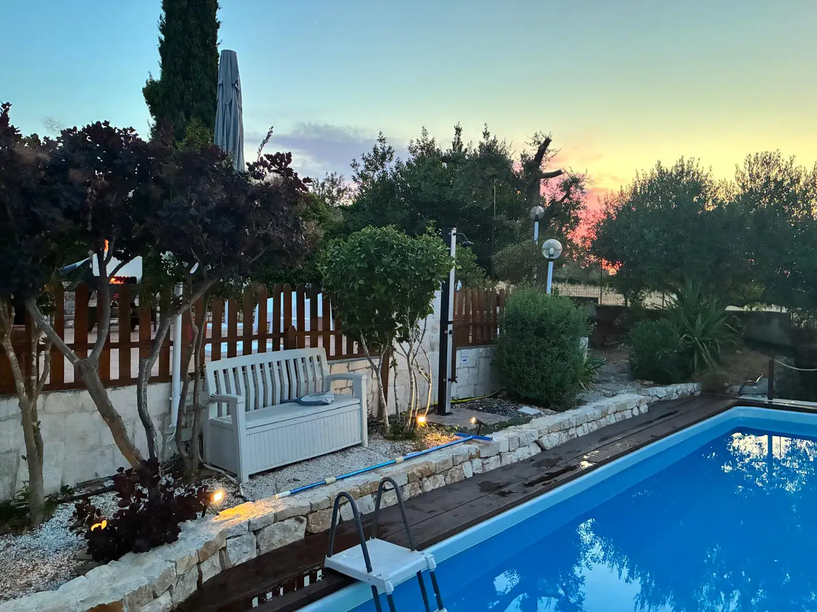 Piscina privata al tramonto con panchina, illuminazione e ulivi